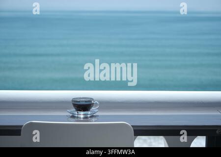 transparente Tasse mit schwarzem Kaffee auf dem Tisch vor dem Strand und dem offenen Meer Stockfoto