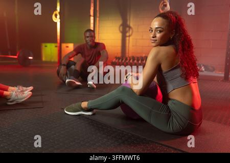 Verschiedene Partner, die auf Matten im Fitnessstudio ruhen, Frau, die sich auf einen lila Medizinball lehnt und einen grauen BH trägt Stockfoto