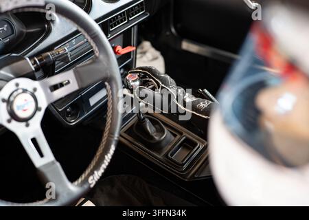 Kemptthal, Zürich, Schweiz, 6. September 2026. Fahrer in Rennanzug und Handschuhen hält den Schaltknauf der Datsun-Handschaltung im Cockpit eines Oldtimer-Rennwagens Stockfoto