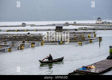 Lake Batur, Bali, Indonesien, 27. März 2026. Ein Bootsführer paddelt an schwimmenden Fischkäfigen und Arbeitsplattformen auf dem Lake Batur vorbei. Stockfoto