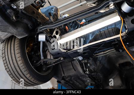 Detaillierte Niedrigwinkelaufnahme von Vorderradaufhängungshebeln, Lenkungsgestellen und Reifen an einem Fahrzeug, das in einer Werkstatt auf einem Hebewerkzeug steht. Stockfoto