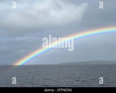 Lebendiger Regenbogen über einem See unter dramatischen Wolken mit einer fernen Uferlinie Stockfoto