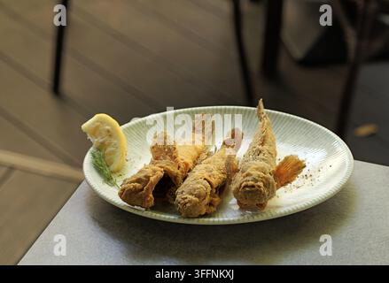 Knusprig gebratener ganzer Butt, paniert und gewürzt, angeordnet auf einem gestreiften Teller mit einer frischen Zitronenscheibe und einem Dillzweig, bereit als Meeresfrüchte-Mahlzeit oder Ap Stockfoto