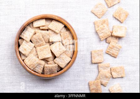Kannellencrunch-Plätzchen, Frühstücksgetreide in Holzschüssel auf Leinen. Flache Stücke aus Vollkorn- und Reismehl, mit Rillen. Foto Stockfoto