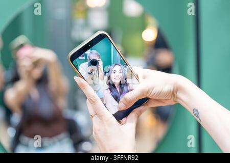 Hände halten ein Smartphone, das die Selfie-Reflexion einer Frau und eines Mannes zeigt, die fotografieren Stockfoto