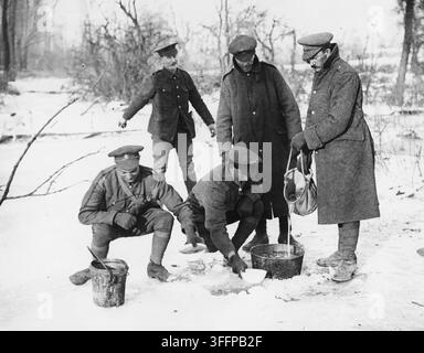 Soldaten, die Wasser aus einem gefrorenen Bach holen, Westfront, während des Ersten Weltkriegs. Diese Fotografie zeigt eine Gruppe von Soldaten, die auf dem Eis über einem kleinen Bach stehen. Sie haben ein Loch ins Eis geschlagen und zwei der Männer verwenden Schüsseln, um Wasser unter dem Eis zu schöpfen und Eimer zu füllen. Zwei der Männer tragen Wintermäntel, aber sie alle sehen kalt aus und haben sehr unzureichendes Schuhwerk für die Bedingungen. [Original lautet: 'Wasser aus einem Loch im Eis holen.'] Stockfoto