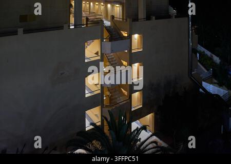 Nachtliche Nahaufnahme-Perspektive einer mehrstöckigen Wohnanlagefassade mit warmer Beleuchtung und Treppenhäusern Stockfoto