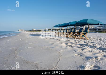 Reihe leerer Strandliegen unter blauen Sonnenschirmen am weißen Sandstrand von Panama City Beach, Florida, USA. Ruhiges Meer, klarer blauer Himmel und friedliche Küste Stockfoto