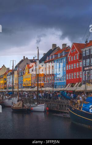 Nyhavn-Kanal in Kopenhagen, Dänemark, gesäumt von farbenfrohen historischen Stadthäusern und festgemachten Booten unter dramatischen Gewitterwolken Stockfoto