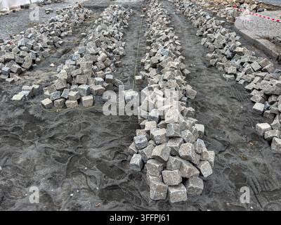 Reihen von grauen Granitpflastersteinen und Kopfsteinpflaster, die auf einer sandigen Baustelle gestapelt sind. Straßenneubauprozess, Straßenrenovierungsarbeiten, urban Stockfoto