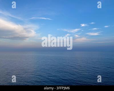 Friedliche und weitwinklige Ansicht des ruhigen blauen Meeres, das unter einem klaren Himmel mit weichen weißen Wolken auf den Horizont trifft, ideal für Hintergrund oder Reisekonzept Stockfoto