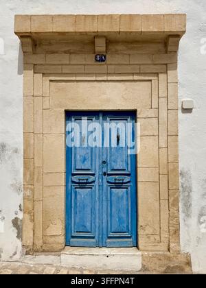 Traditionelle blaue Holztür, umrahmt von einem Steinrahmen in der UNESCO-geschützten Medina von Sousse, Tunesien. Stockfoto