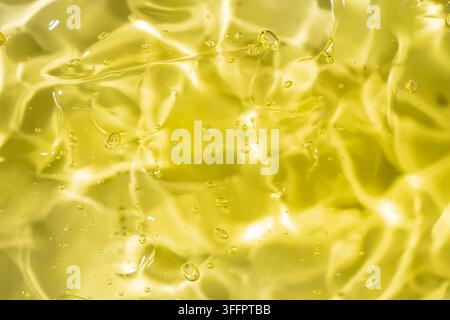 Nahaufnahme von durchscheinendem gelbem Gel mit verstreuten Luftblasen, glänzenden Reflexionen und flüssigen Wellen, die eine lebendige abstrakte Textur für Kosmetik erzeugen Stockfoto