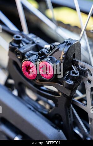 Detaillierte Nahaufnahme einer Motorradscheibenbremse mit roten Schrauben, Metallrotor, Speichen und hydraulischem Kabel, die wesentlichen Radkomponenten und mich zeigend Stockfoto