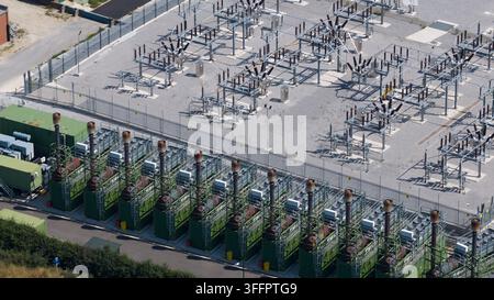 Luftaufnahme eines Umspannwerks neben einer Kraftwerksanlage, das Transformatoren, Schalteranlagen, Übertragungsanlagen, Kühlgeräte und ein Stockfoto