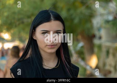 Eine junge Frau mit langen dunklen Haaren schaut mit ernstem Ausdruck im Freien in die Kamera. Stockfoto