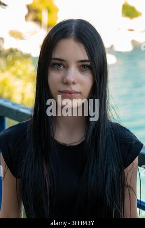 Junge Frau mit langen schwarzen Haaren schaut direkt in die Kamera im Freien. Stockfoto