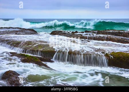 Kraftvolle Meereswellen schlagen gegen die felsige Küste am Thousand Steps Beach in Laguna Beach, Kalifornien. Kaskadierendes Wasser fließt über strukturierte Felsen creat Stockfoto