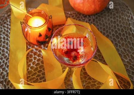 Gruseliges Halloween-Stillleben mit einem blutroten Cocktail, schwebenden Beeren, die unheimlichen Augen ähneln, einer flackernden Kerze Stockfoto