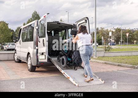 Rollstuhlnutzer verlässt ein behindertengerechtes Fahrzeug mit Unterstützung eines Assistenten über eine barrierefreie Rampe. Stockfoto
