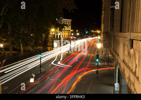 Langzeitbelichtete Nachtszene mit Verkehr, die dynamische weiße und rote Lichtspuren auf einer mehrspurigen Stadtavenue in der Nähe einer Straßenecke und eines historischen Gebäudes zeigt. Stockfoto