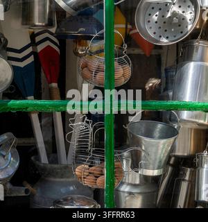 Grünes Holzfenster mit geöffneten Fensterläden, das eine Auswahl an Metallkrügen, Kannen und Küchenutensilien zeigt, die ordentlich darin angeordnet sind. Stockfoto