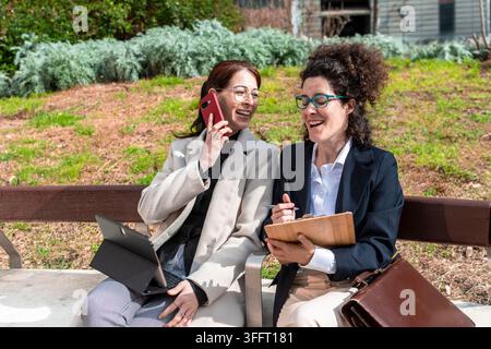 Professionelle Frauen, die im Freien zusammenarbeiten und während eines Telefonats lachen Stockfoto