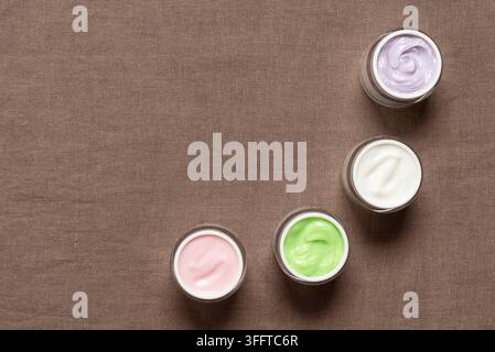 Farbige Kosmetikcremes im Glas auf braunem Textilhintergrund, Oberansicht, Flat Lay, Kopierraum Stockfoto