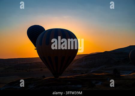Silhouetten von Heißluftballons, die bei Sonnenaufgang über der Landschaft Kappadokias schweben Stockfoto