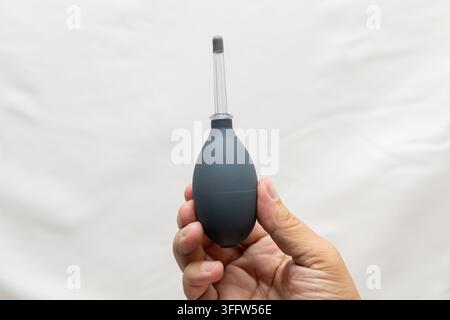 Hand, die einen schwarzen Gummiluftblaser mit transparenter Düse gegen einen hellen Hintergrund hält, isolierte Komposition mit großzügigem Kopierraum Stockfoto