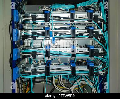 Rückseite von Netzwerkservern im Rack, montiert auf Schlitten mit Kabelanschlüssen. Schwarze Stromkabel, Lüftungsschlitze, zyanblaue Glasfaserkabel, die in Befestigungen fixiert sind Stockfoto