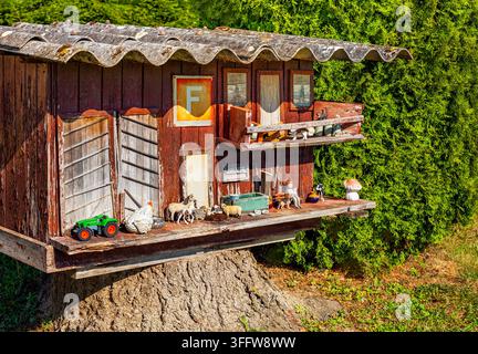 Bezauberndes Miniatur-Holzhaus einer Schweizer Farm, gebaut auf einem Baumstumpf mit Spielzeugtieren und grünem Traktor Stockfoto