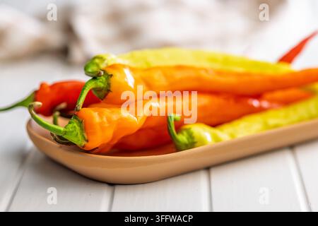 Hellorange, gelbe und rote Chilischoten, die auf einem kleinen Teller arrangiert sind, zeigen glänzende Haut, frische Stängel und lebendige Farben zum Kochen, Würzen Stockfoto
