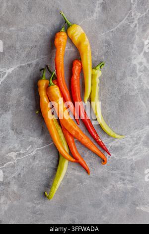 Lebendige lange Chilischoten in Rot, Orange, Gelb und Grün, arrangiert auf einer Marmorfläche, ideal für Lebensmittelfotografie, Rezeptbilder, Kochkonzepte Stockfoto