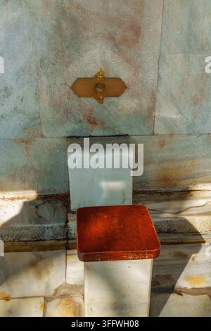 Antiker Messing-Wasserhahn, der an einer verwitterten Marmorwand an einem alten Brunnen in Istanbul, Türkei, montiert ist. Traditionelles architektonisches Detail im osmanischen Stil w Stockfoto