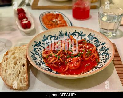 Meeresfrüchte in einer mediterranen Tomatensauce. Ein köstliches Gericht auf einem Keramikteller auf einer weißen Serviette, eine Scheibe Handwerksbrot. Stockfoto