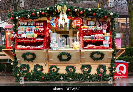 Iasi, Rumänien – 4. Januar 2026: Ein traditioneller Holzstand auf dem Weihnachtsmarkt, geschmückt mit Kiefernkränzen und roten Kugeln, der bunte Lutscher verkauft Stockfoto