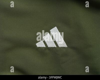 Tambow, Russische Föderation - 03. September 2026 Ein weißes besticktes Adidas-Leistungslogo auf einem dunklen khakifarbenen Sportbekleidungsstoffhintergrund. Stockfoto