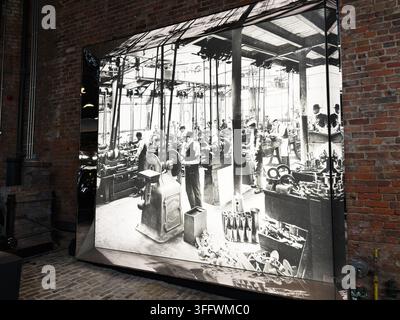 Manchester, UK - 02. Juli 2026: Große schwarz-weiße Museumsaustellung eines historischen Fabrikinnerraums von Manchester mit Arbeitern und Maschinen. Stockfoto