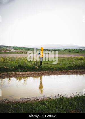 Der junge Mann in der gelben Jacke steht am Wasser an der Straße. Stockfoto