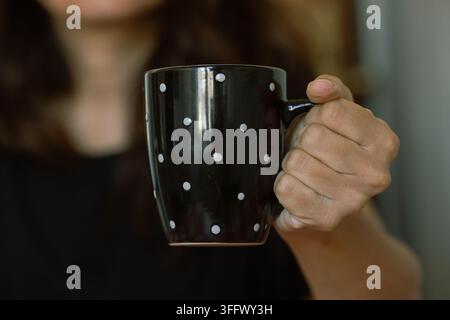 Eine Hochwinkel-Makrofotografie fängt eine dunkle, möglicherweise schwarze, Keramiktasse mit einem hellbeigen Tupfenmuster ein Stockfoto