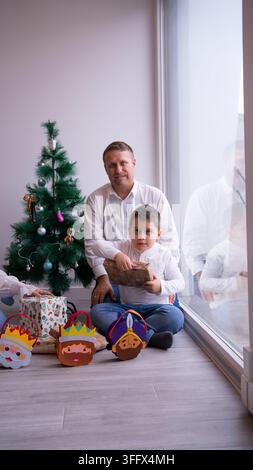 Glückliche Familie sitzt auf dem Boden neben einem Weihnachtsbaum und packt Geschenke aus Stockfoto