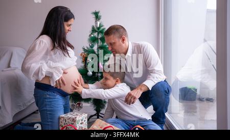Familie zeigt Zuneigung zum Bauch der schwangeren Mutter während der Weihnachtsfeiern zu Hause Stockfoto