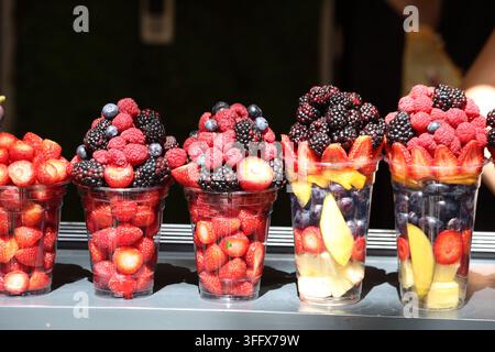 Frische Beeren- und gemischte Obstsalatbecher, die in einem Marktstand zum Verkauf angeboten werden Stockfoto