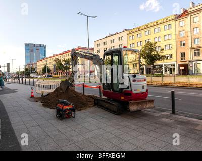 Danzig, Polen - 28. Juli 2026: Kleine Kompaktbagger gräbt Loch auf belebter städtischer Straße für Wartung der Versorgungsinfrastruktur und Untergrundreparatur-Bauprojekt Stockfoto