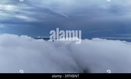 Luftaufnahme von dicken weißen Wolken, die die Landschaft unter einem dunkelblauen stürmischen Himmel in der Regierungsbezirk Sukabumi, West-Java, Indonesien bedecken. Stockfoto