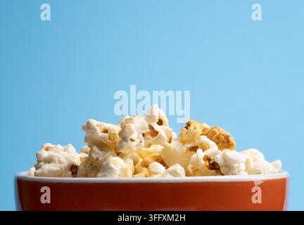 Frisches Bio-Popcorn in einer orangefarbenen Schüssel auf blauem Hintergrund mit Platz für Ihren Text Stockfoto