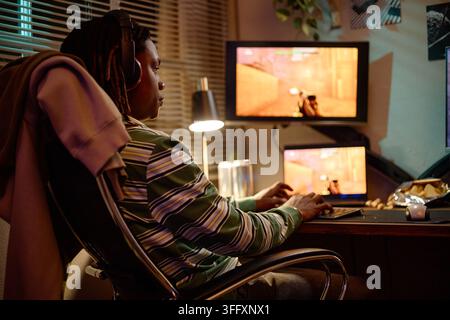 Konzentrierter schwarzer Mann trägt Kopfhörer und spielt Videospiele am Computer Stockfoto
