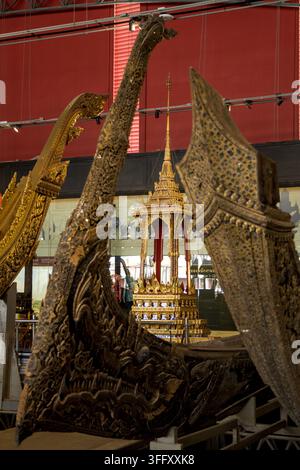 Aufwendig verzierter goldener, gestufter Throntempel umgeben von traditionellen geschnitzten Holzzeremonialbooten, die das königliche thailändische Erbe präsentieren. Stockfoto