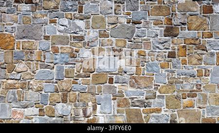 Massive Steinmauer aus unregelmäßigen flachen mehrfarbigen Steinen auf Beton. Vollformat. Hintergrund und Textur. Stockfoto